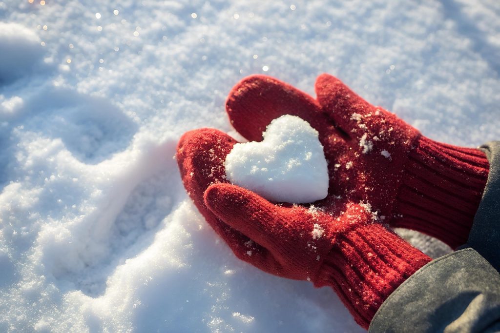 Hands wearing red gloves holding a snow heart symbolizing love and warmth